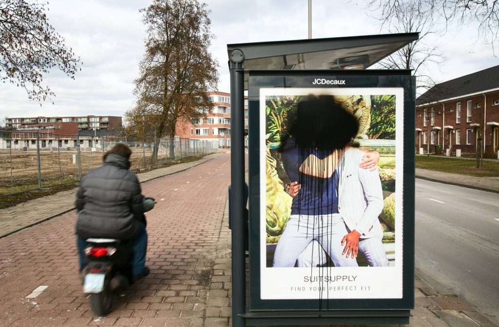 Dezelfde reclame van Suitsupply, nu is het besmeurd met zwarte verf. Hierdoor zijn de hoofden van de mannen niet meer te zien.